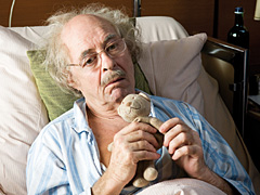 Verwirrter Alter im Altenheimbett hält einen Teddybären in seinen Händen