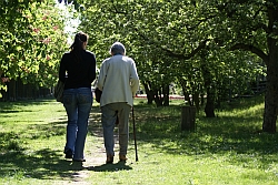 Eine Frau spaziert mit Seniorin durch Garten