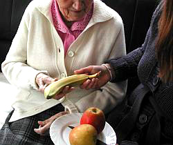 Eine Betreuerin reicht einer alten Frau eine Banane.